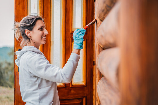 Woman with paint brush repairing wooden house. The process of painting the wooden wall of the house. Paint brush in hand close-up, wood texture and paint. Do it yourself. 