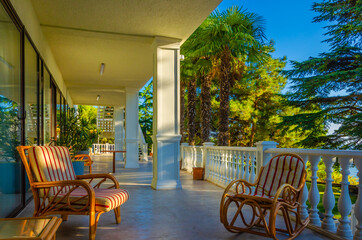The veranda of the house with armchairs on the background of palm trees.