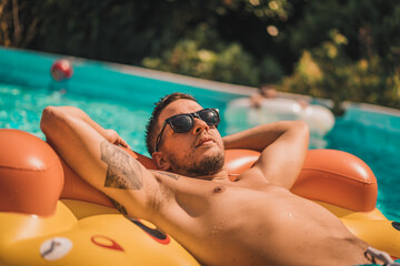 Handsome young man enjoying summer time in pool on the inflatable mattress in the swimming pool having fun.