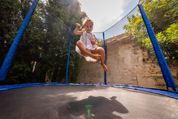 Little happy toddler girl jumping on her trampoline outside on a summer day. Kid jumping on...