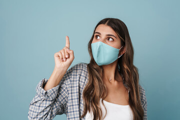 Surprised girl in face mask looking aside and pointing finger upward