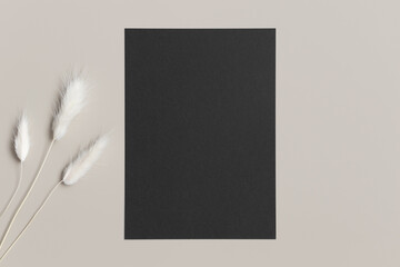 Black invitation card mockup with a lagurus on the beige table. 5x7 ratio, similar to A6, A5.