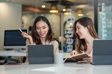 Two asian business woman smile happy while working on a laptop at the office.