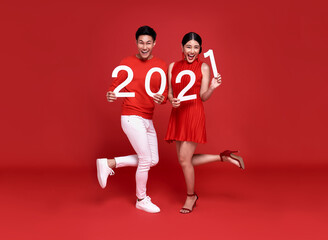 Fototapeta na wymiar Happy asian couple in red casual attire showing number 2021 greeting happy new year with smiles on bright red background.