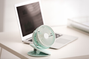 Modern electric fan and laptop on table in office