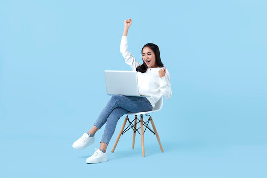 Young woman asian happy smiling celebrate. While her using laptop sitting on white chair isolate on bright blue background.