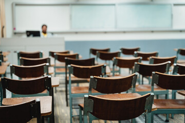 Wooden lecture chairs arranged in the classroom. Empty college classroom with many vintage wooden...
