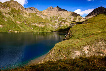 Fototapeta premium Fanealm und Wilder See in Suedtirol, Italy, Alpine pastures with a deep blue lake, green meadows and a blue sky with fleecy clouds, in summer