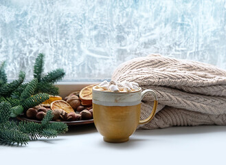 Coffee cup with marshmallows, fir branches, sweater, frosty window. home comfort in snowy cold weather. relax and reading. winter season. Christmas and New Year holiday background