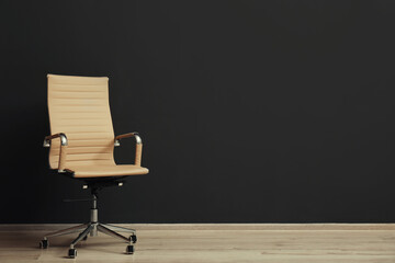 Comfortable office chair near black wall indoors. Space for text