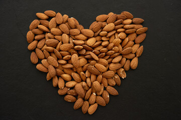 Almond nuts forming a heart-shape on black background.  (selective focus; close-up shot)