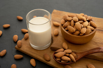 Almond milk with almond in a wooden spoon and bowl on a wooden (selective focus; close-up shot)