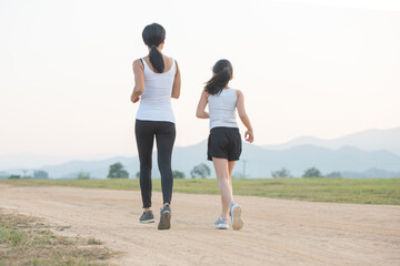 two female runners jogging outdoors in forest in autumn nature..running sporty mother and daughter. woman and child jogging in a park. outdoor sports and fitness family.