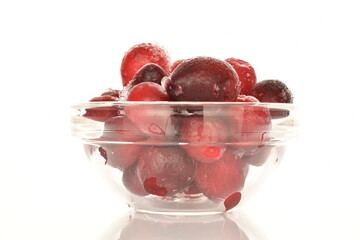 Several berries of red freshly frozen cranberries in a glass dish, close-up, isolated on white.