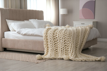 Soft knitted blanket on bed in room. Interior element