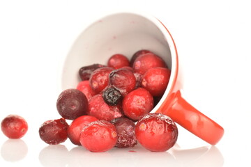 Several organic freshly frozen cranberries with a red cup, close-up, isolated on white.