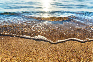 Close up of small sea waves with clear blue water over yellow sand beach at summer sunny shore.