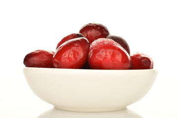 Several berries of red freshly frozen cranberries in a white ceramic bowl, close-up, isolated on white.