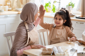 Cheerful Muslim Mom And Daughter Giving High-Five To Each Other In Kitchen