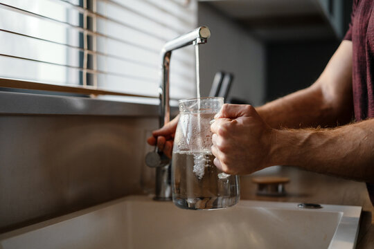 Close up of a man pouring water in the jug from a tap