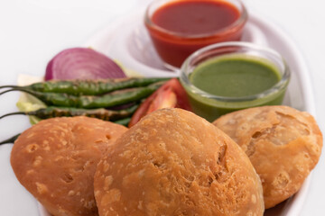 Closeup Of Khasta Masala Kachauri Also Called Pyaj Kachori Or Pyaaz Kachodi Served With Tomato Sauce Green Chutney Onion Mirchi In Platter And Glass Bowls. White Background With Copy Space For Text