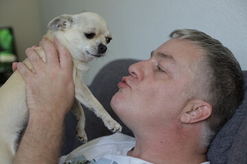 Caucasian man 45 years old kisses his mini beige chihuahua dog
