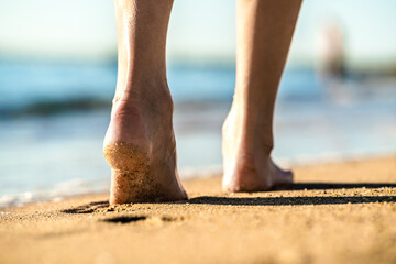 Close up of woman feet walking barefoot on sand leaving footprints on golden beach. Vacation, travel and freedom concept. People relaxing in summer.