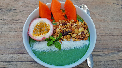 Exotic, balinese style granola fruit bowl with Papaya, granola, coconut, passion fruit on wooden,...