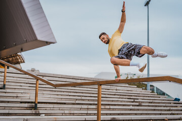 Man doing sports and training outdoors in city. Man jumping over the fence and working out hard. Parkour elements in workout.  - Powered by Adobe