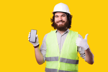 Portrait of happy engineer man holding smartphone and showing thumb up gesture.