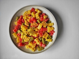 Colorful pasta in different shapes in light gray plate on a light gray background, closeup, horizontal