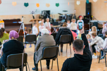 Parents at the performance of children in kindergarten or school. Children on stage. Many parents are watching the kids performance in the hall during Chistmas holiday, blurry