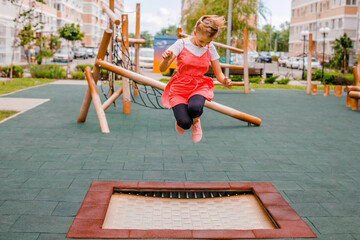 Fototapeta na wymiar A teenage girl in a summer dress plays on the playground near her home