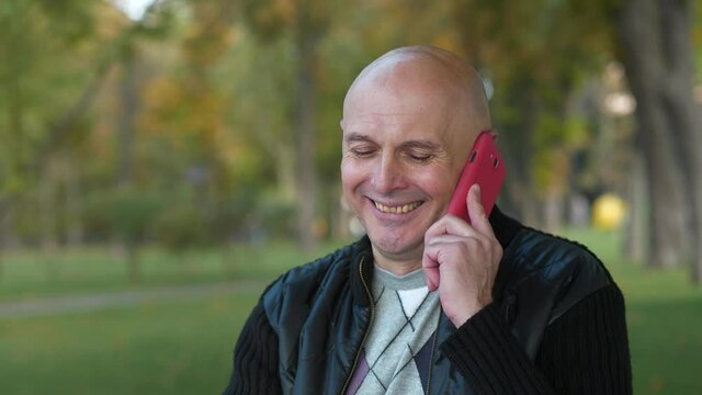 Smiling bald senior man talks on smartphone