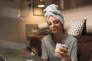 girl applying cosmetic face mask, sitting in her room , using mobile phone