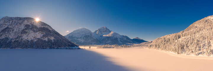 snow-covered frozen lake heiterwangersee in winter with morning sun on the mountain ridge with...