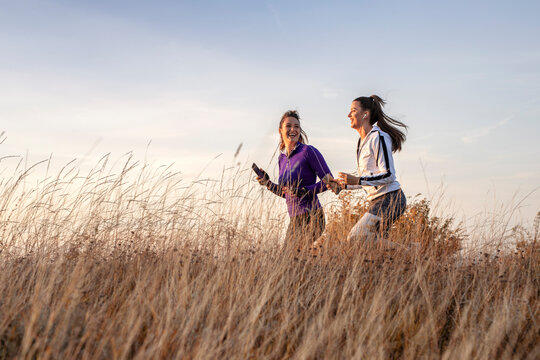Young and happy best female friends in sportswear jogging together in nature