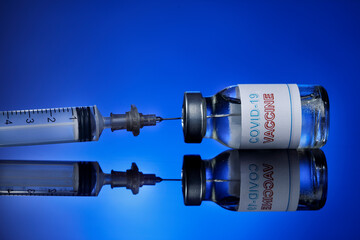 prelievo del  vaccino anti-covid con una siringa da una filetta di vetro, isolato su sfondo blu...