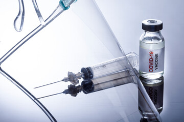 filetta di vetro del vaccino anti-covid  con una siringa e posti sulla superfice riflettente del tavolo di un  laboratorio - obrazy, fototapety, plakaty