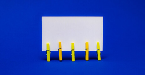 On bright blue background on yellow clothespins white blank card with copy space