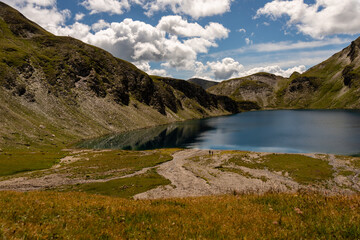 Naklejka na ściany i meble Fanealm und Wilder See in Suedtirol, Italy, Alpine pastures with a deep blue lake, green meadows and a blue sky with fleecy clouds, in summer