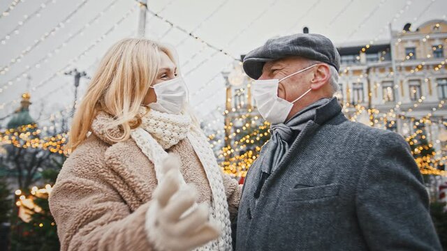 Close up of senior couple embracing outdoors during walk in city center on Christmas wearing protective medical masks