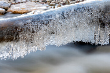 Branch covered in ice over fast flowing river water
