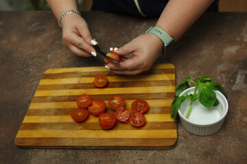 The hands of the woman housewife are cutting cherry tomatoes on a wooden cutting board.