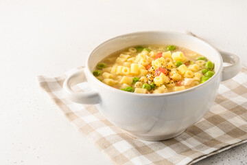 Tasty soup with ditalini pasta, peas, ham on white table. Close up. Copy space.