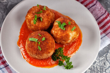 Delicious hot italian arancini - rice balls stuffed with cheese in tomato sauce, in a plate on an old wooden table