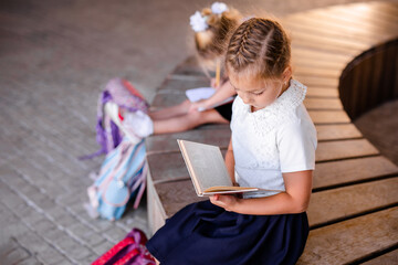 Fototapeta na wymiar Little blonde girl in school uniform studying at the park
