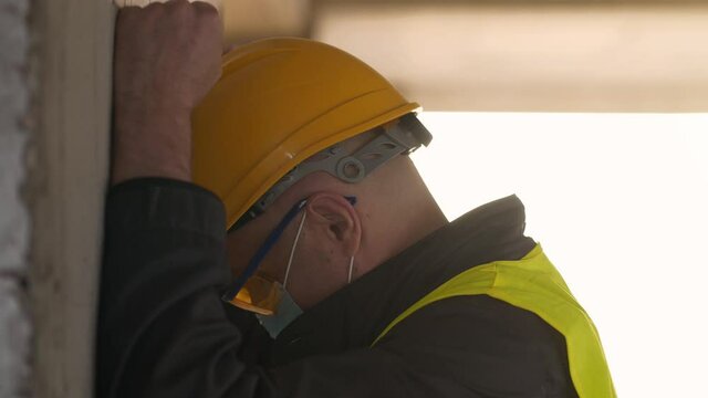 Slow Motion Stressed workman stands on construction site and knocks his hands and head against the wall, self-condemnation, self-torture, industrial accident