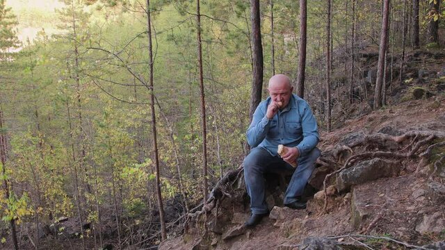 A man in jeans sits on the side of a quarry and eats a baguette. A wonderful view of the natural landscape. Tourist sightseeing. Picturesque expanses of the country. Summer travel at sunset. 4K.