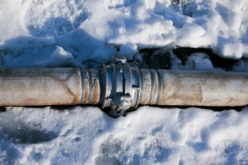 Winter. Everything is covered with snow. Leak in the connection of pipes pumping water out of the...